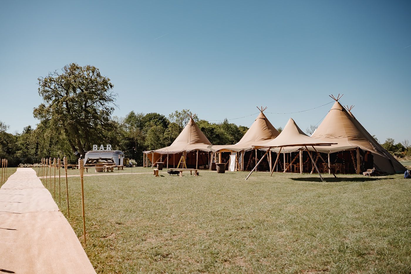 Wedding celebration with multiple tipi tents set up on grassy field as guests mingle outdoors.