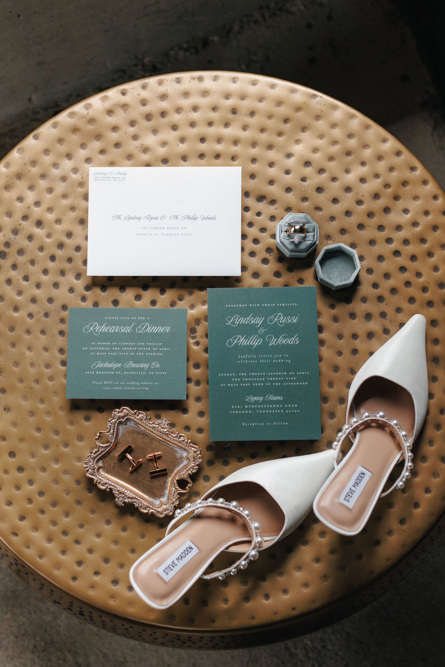 Wedding invitation cards and a pair of elegant white bridal shoes arranged on a textured round table surface.