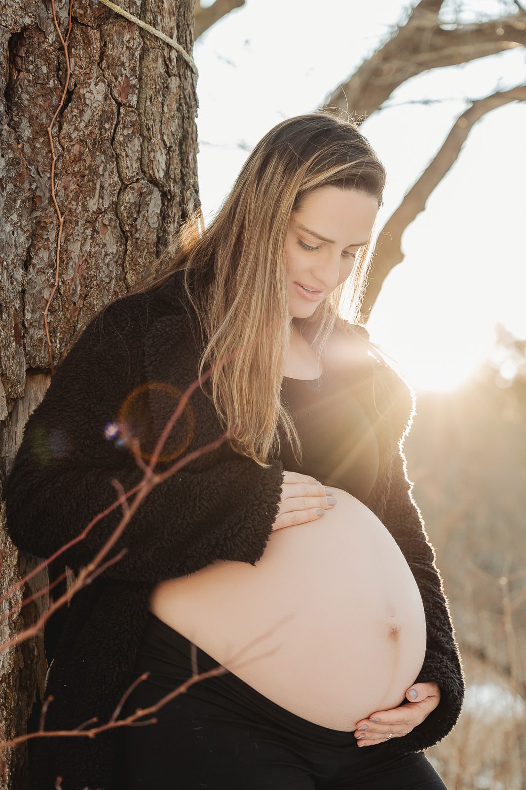 A maternity portrait with beautiful sunlit glow showing a pregnant belly against a natural outdoor winter setting.