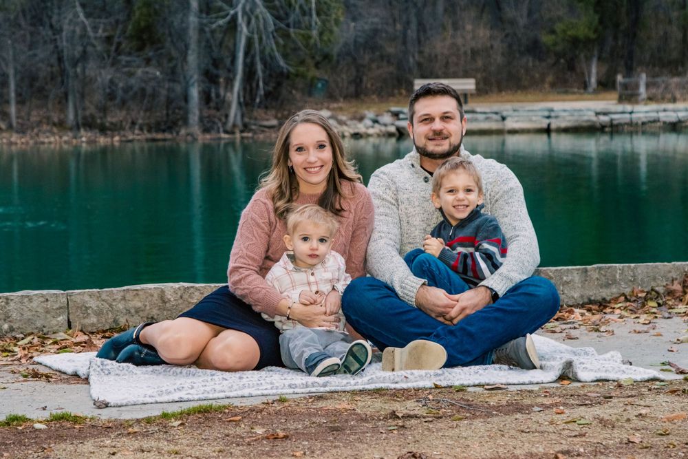 Family sitting on blanket by turquoise lake with winter landscape in background.