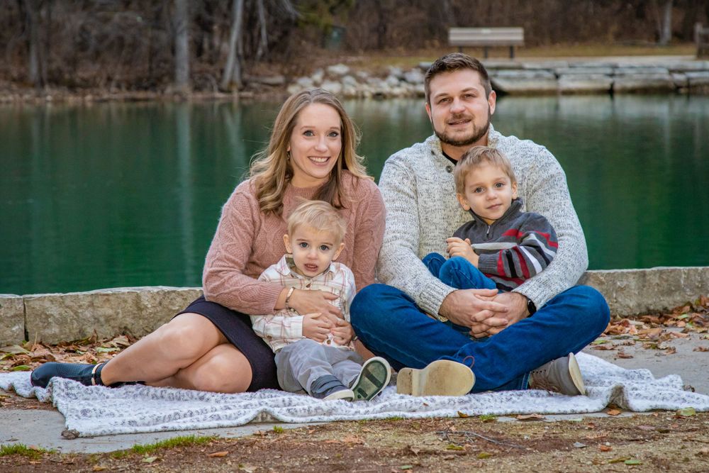 Family sits together on blanket by turquoise lake during fall season photoshoot.