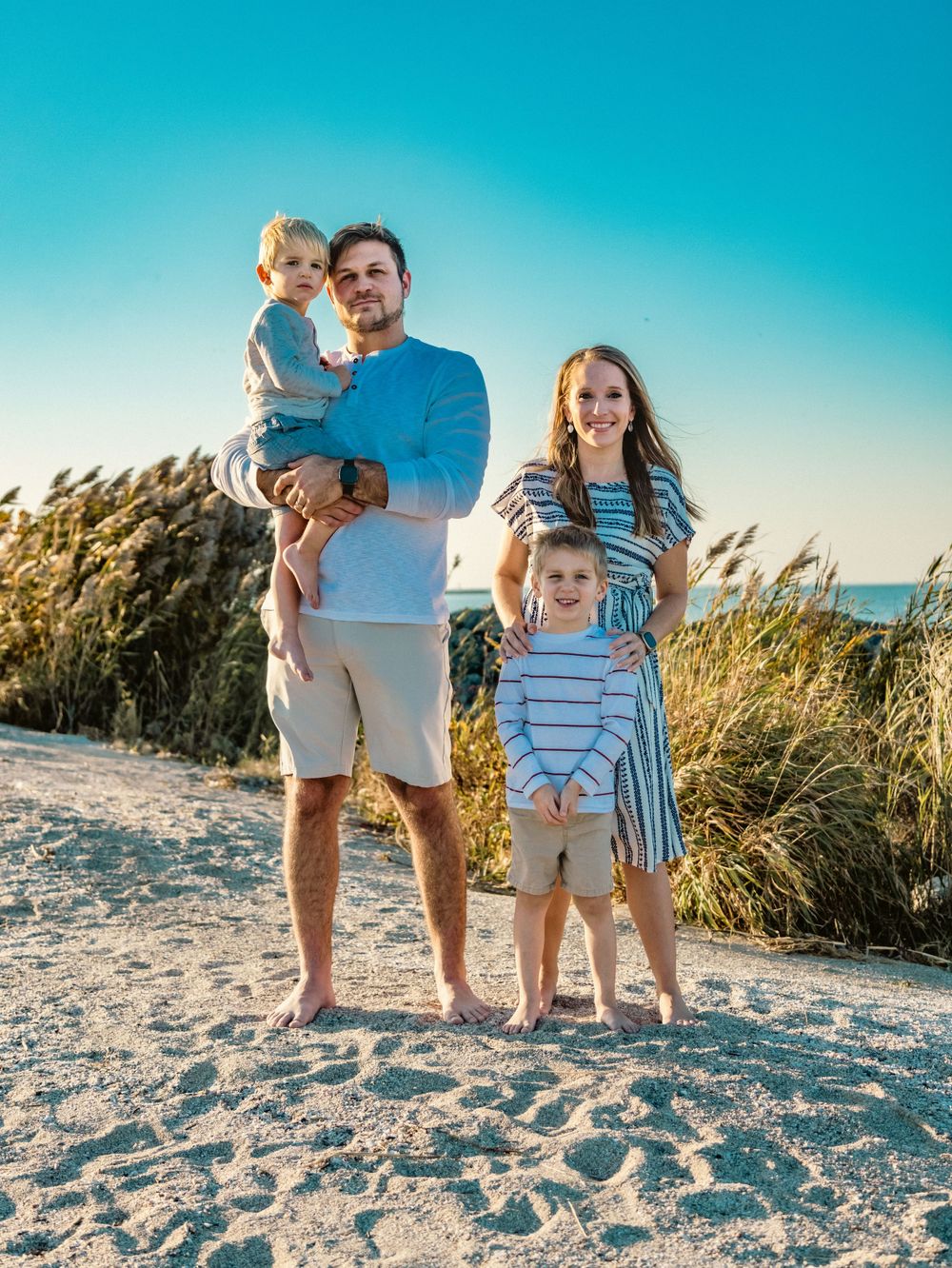 Family portrait on beach with golden sea oats and bright blue sky.