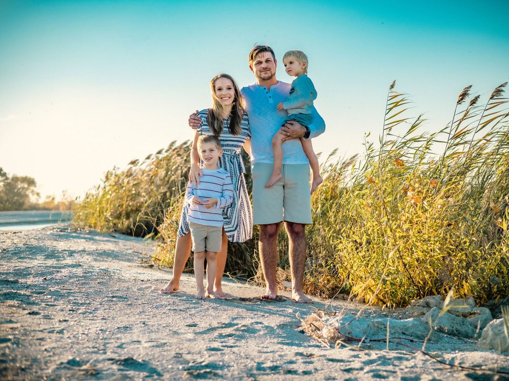Family stands together on sandy coastal path during sunset photoshoot.