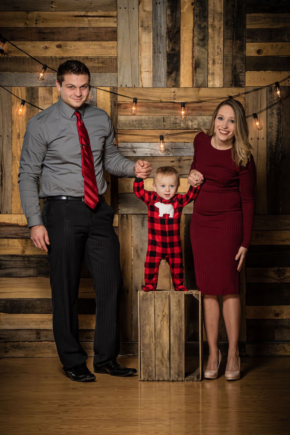 Family holiday portrait against rustic wooden wall with string lights.