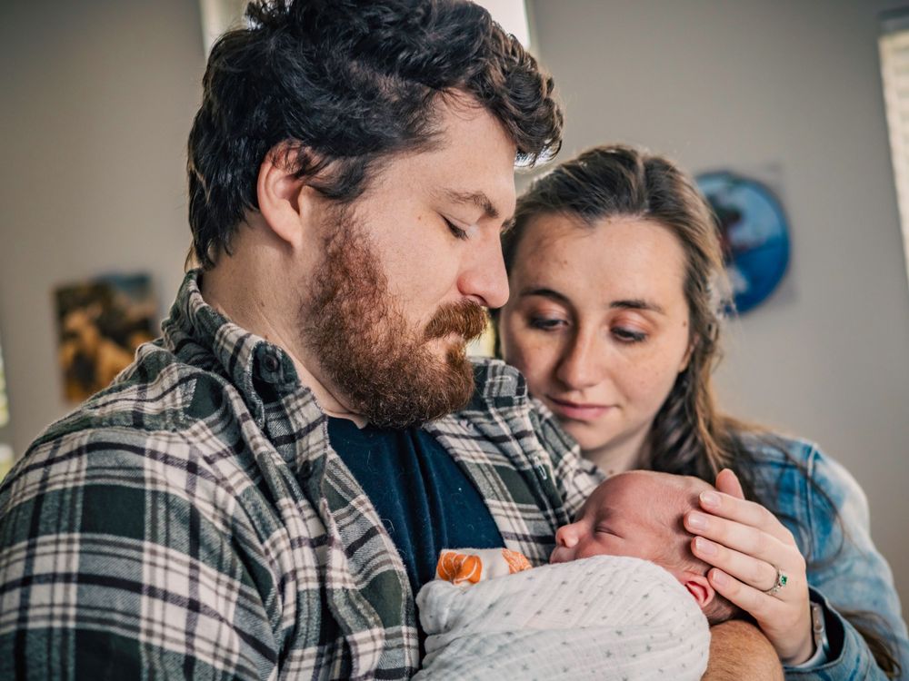 Couple gazes lovingly at their swaddled newborn baby in their home.