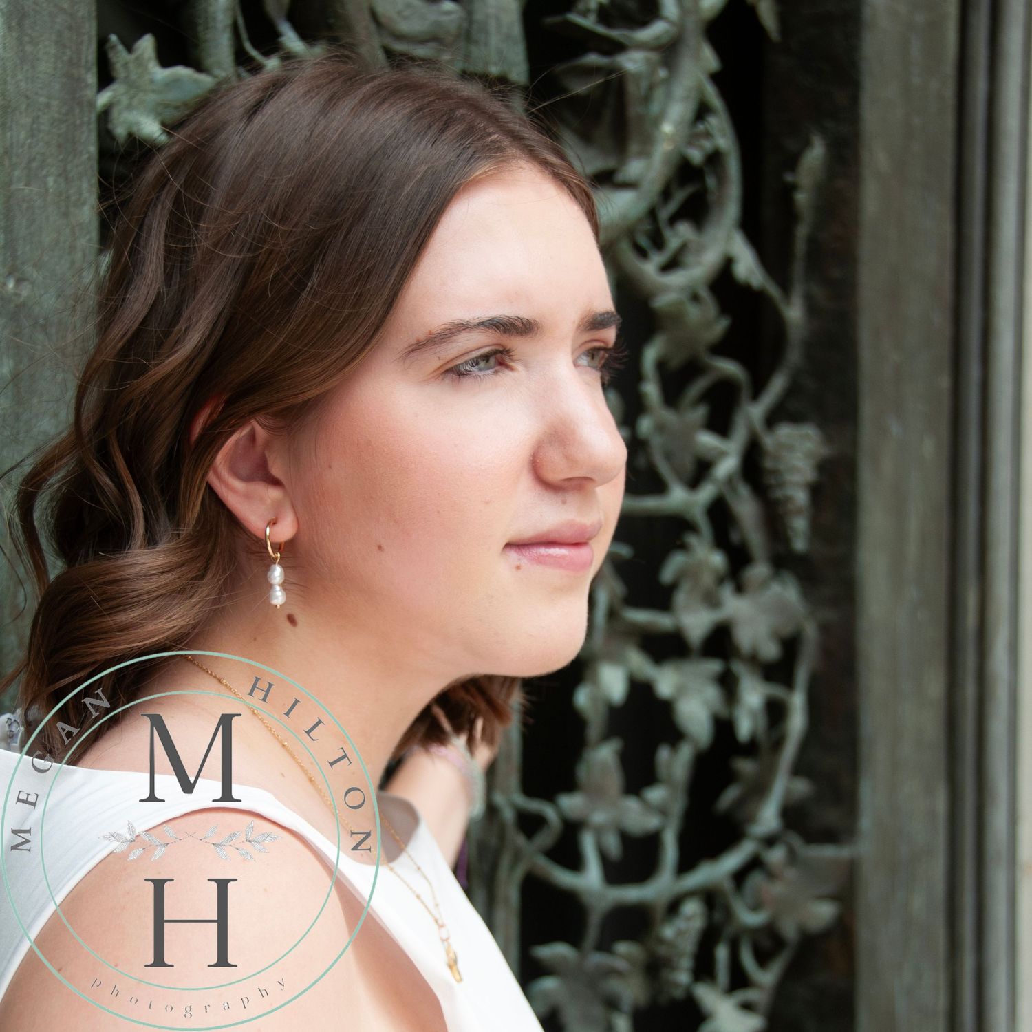 Profile view of a young girl wearing dangling earrings looking thoughtfully into the distance against wrought iron grapevine door.