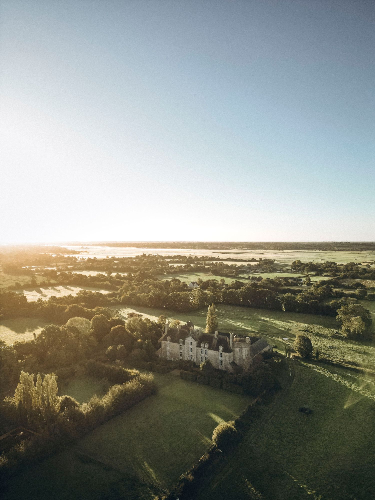 Aerial view of a majestic castle surrounded by green countryside at sunset with golden light casting long shadows.
