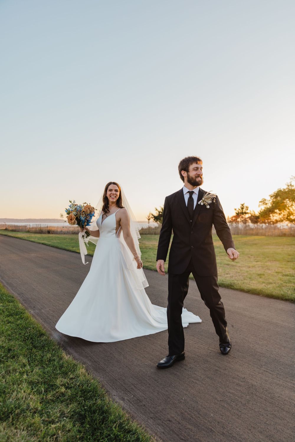 Newlyweds walking together on a rural path at sunset with a white wedding dress and classic black suit.