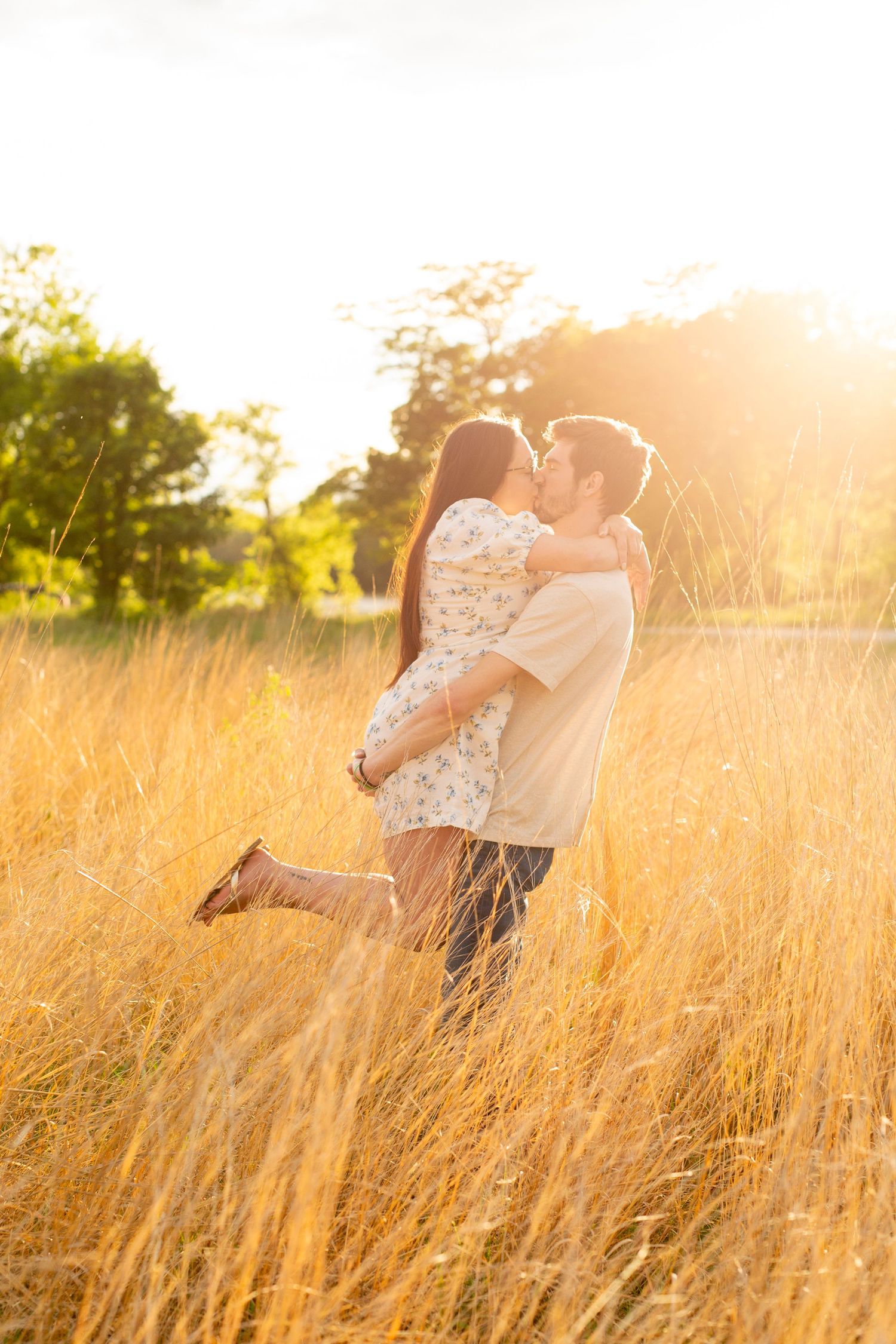 A romantic couple embraces in a sun-lit golden field of tall grass during sunset, creating a dreamy silhouette.