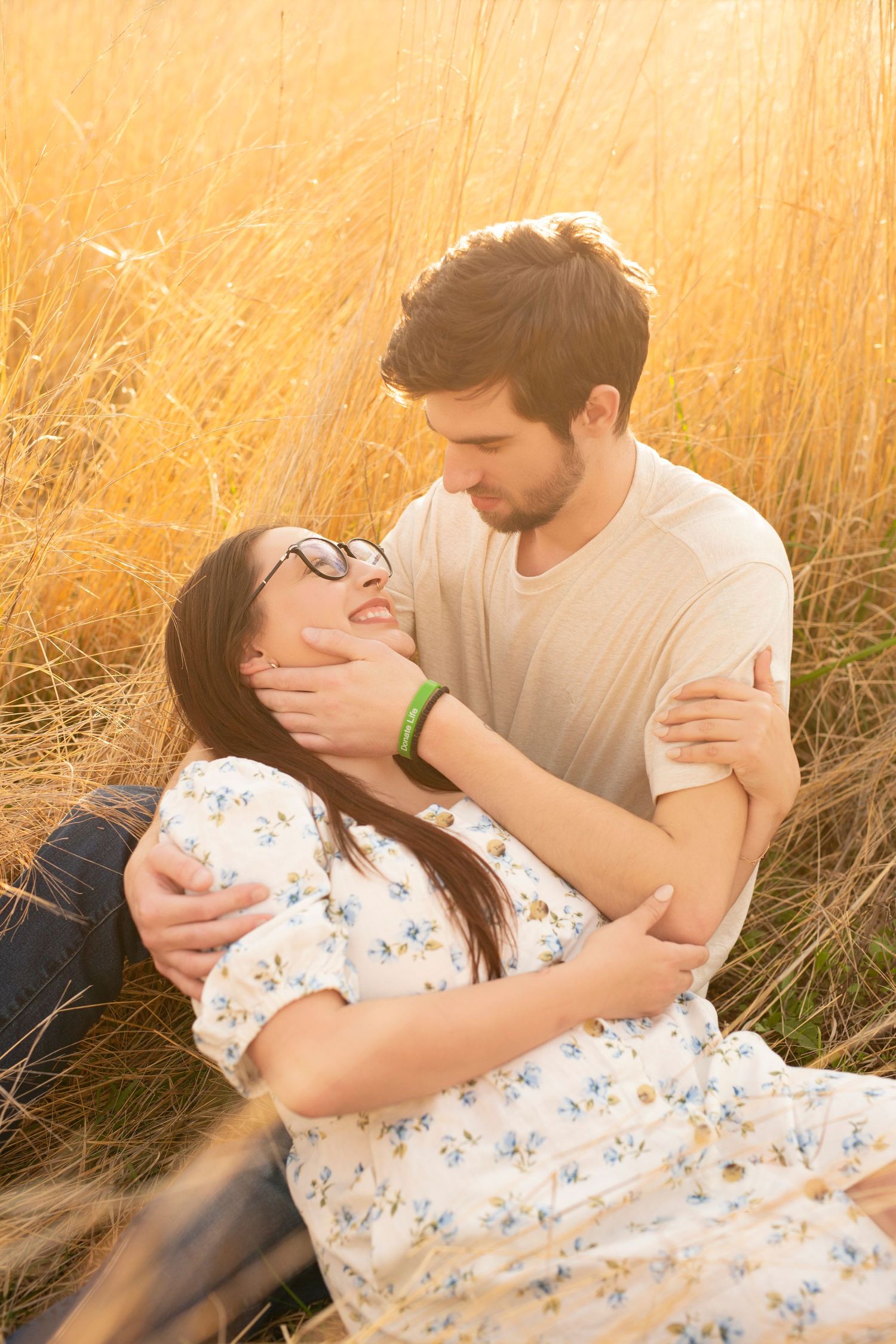 Romantic couple lounging in golden sunlit grass field during sunset portrait session.
