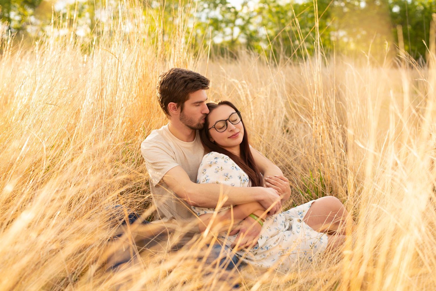 A couple laughing and embracing in golden tall grass during a sunset photo session in the countryside.