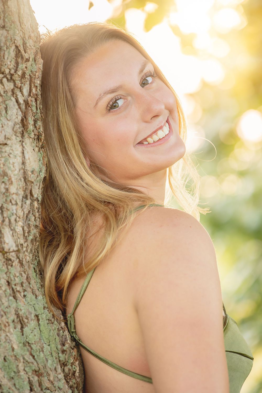 Golden sunlit portrait session against a tree trunk with warm summer lighting and natural backlight.
