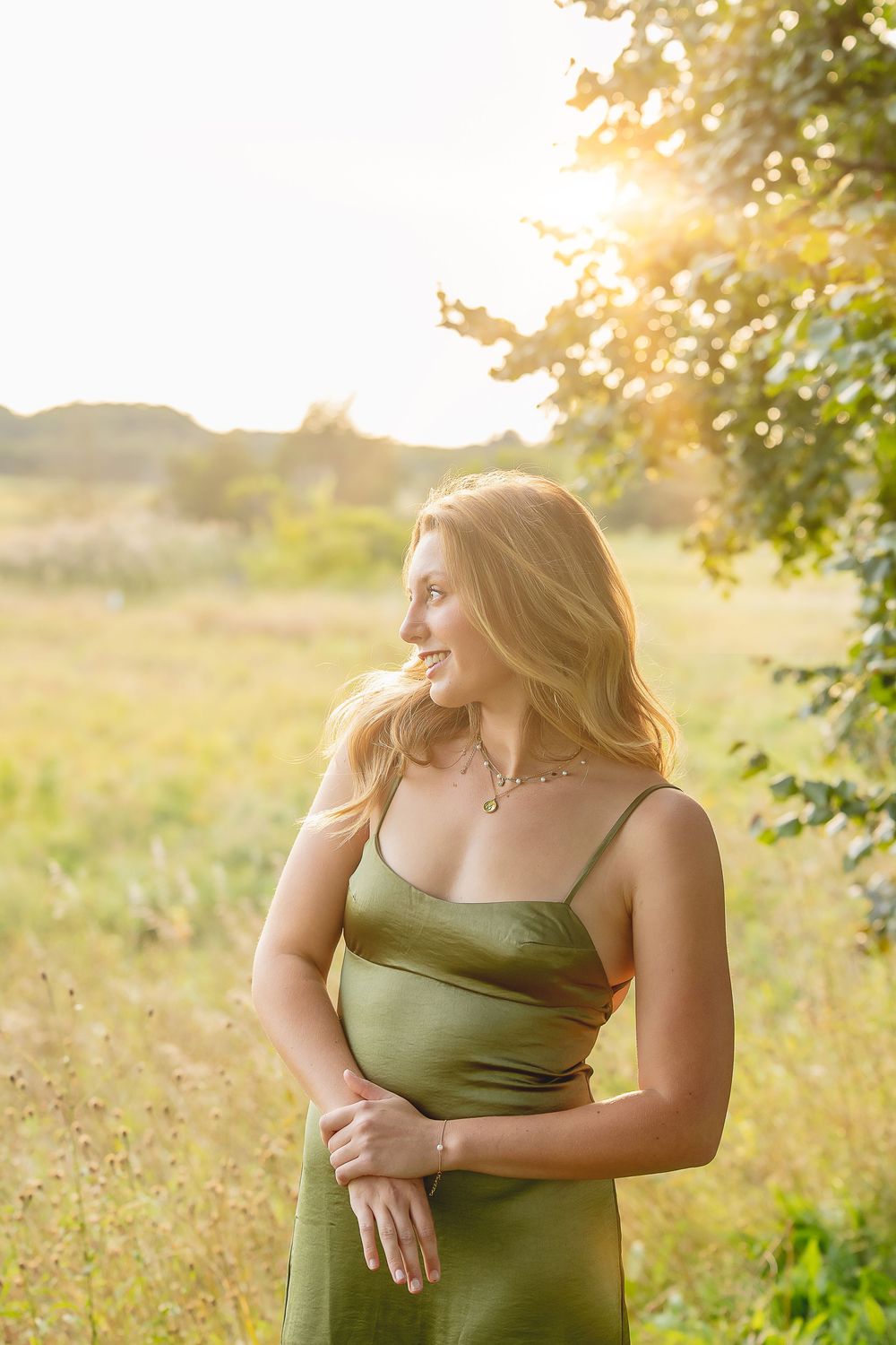 Portrait in an olive green top posed against a dreamy natural sunset backdrop in summer meadow.