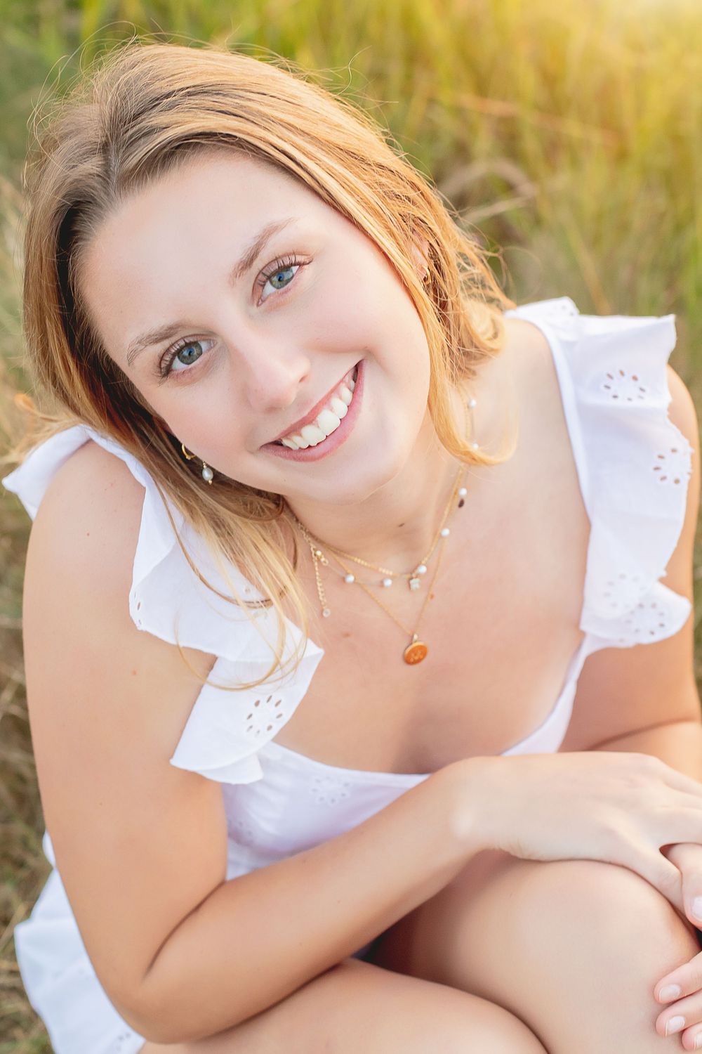 Sunlit outdoor photoshoot with a flowing white summer dress against tall natural grass.