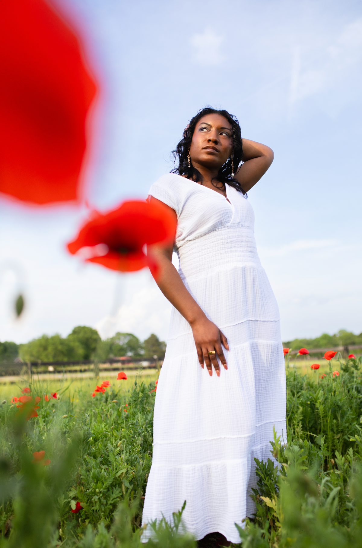 A woman in white dress poses gracefully in a blooming red poppy field at Juniper Creek Farm