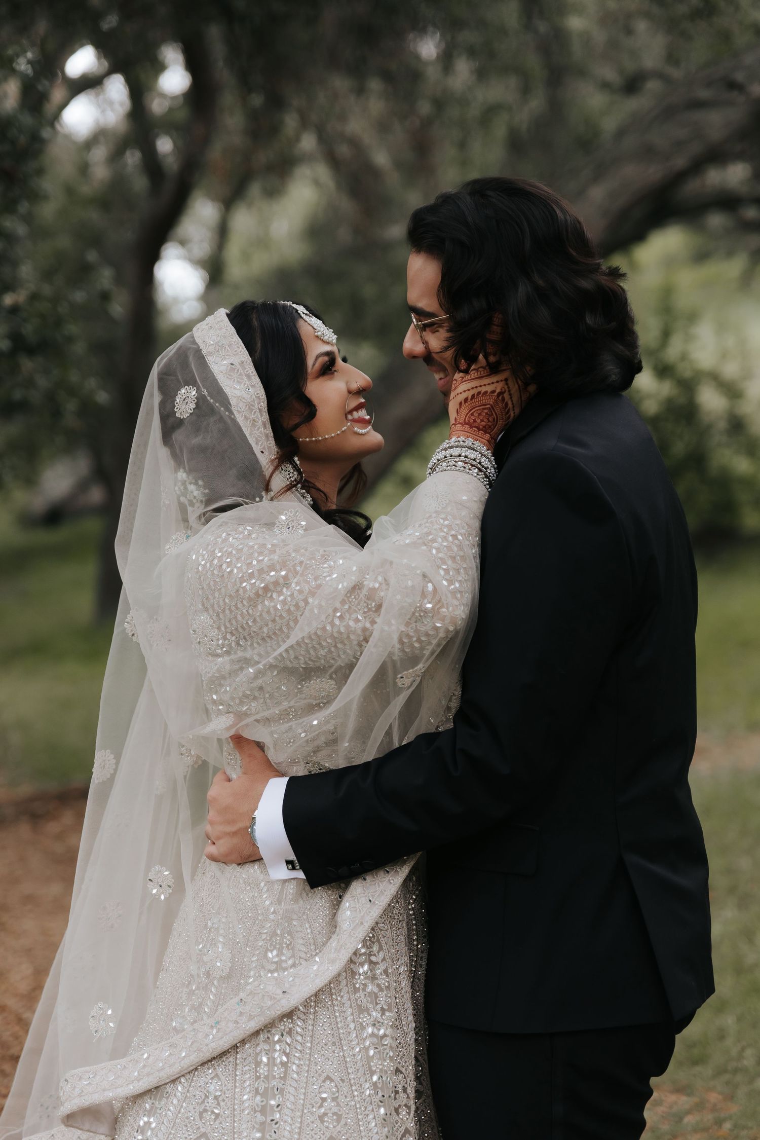 Newlywed couple sharing intimate romantic moments in outdoor garden setting with bride wearing detailed white lace gown.
