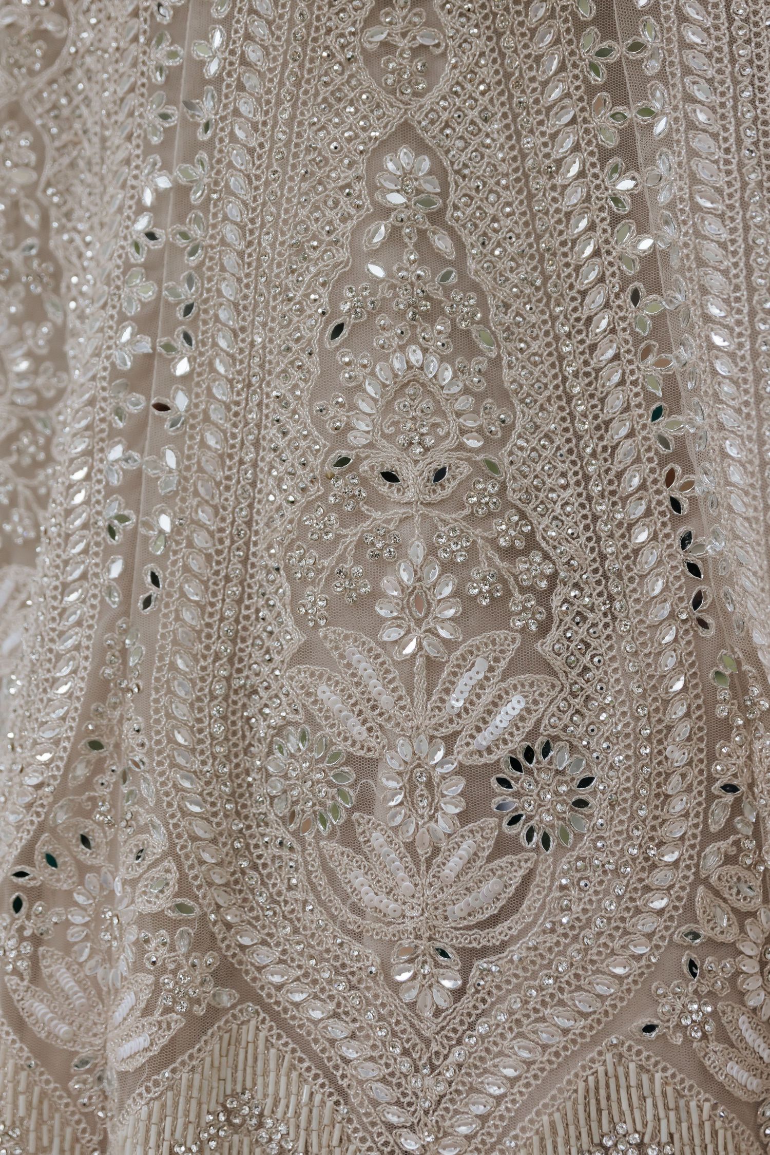 Close-up details of ornate embroidery and beadwork on a white wedding dress fabric.