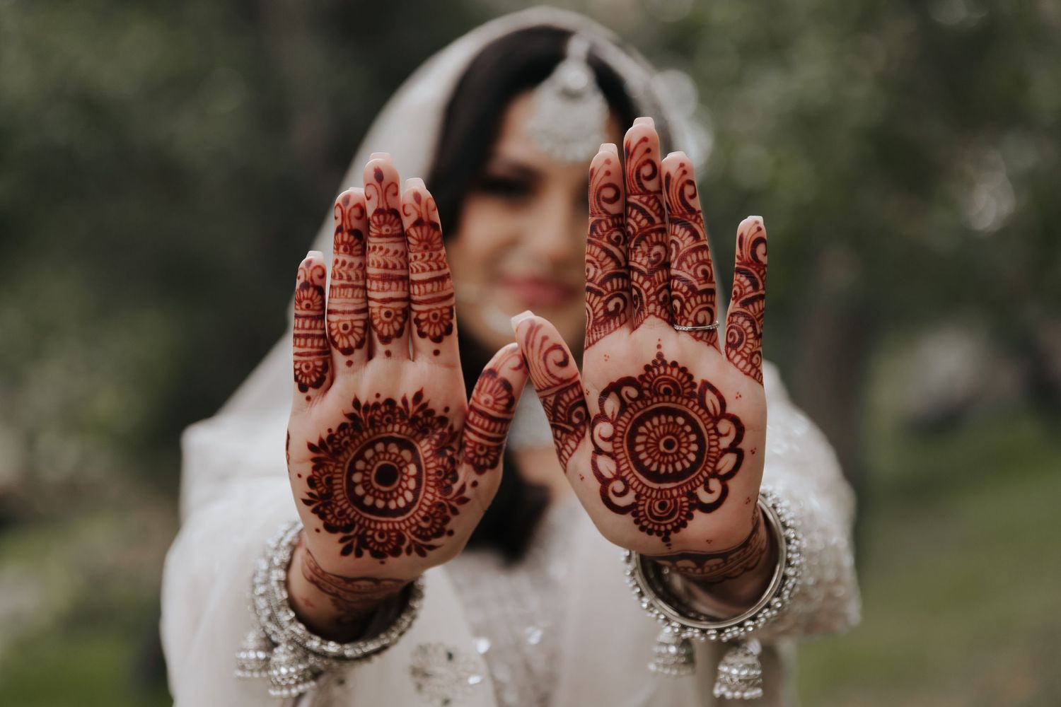 Intricate henna designs displayed on palms of hands with white lace dress sleeves.