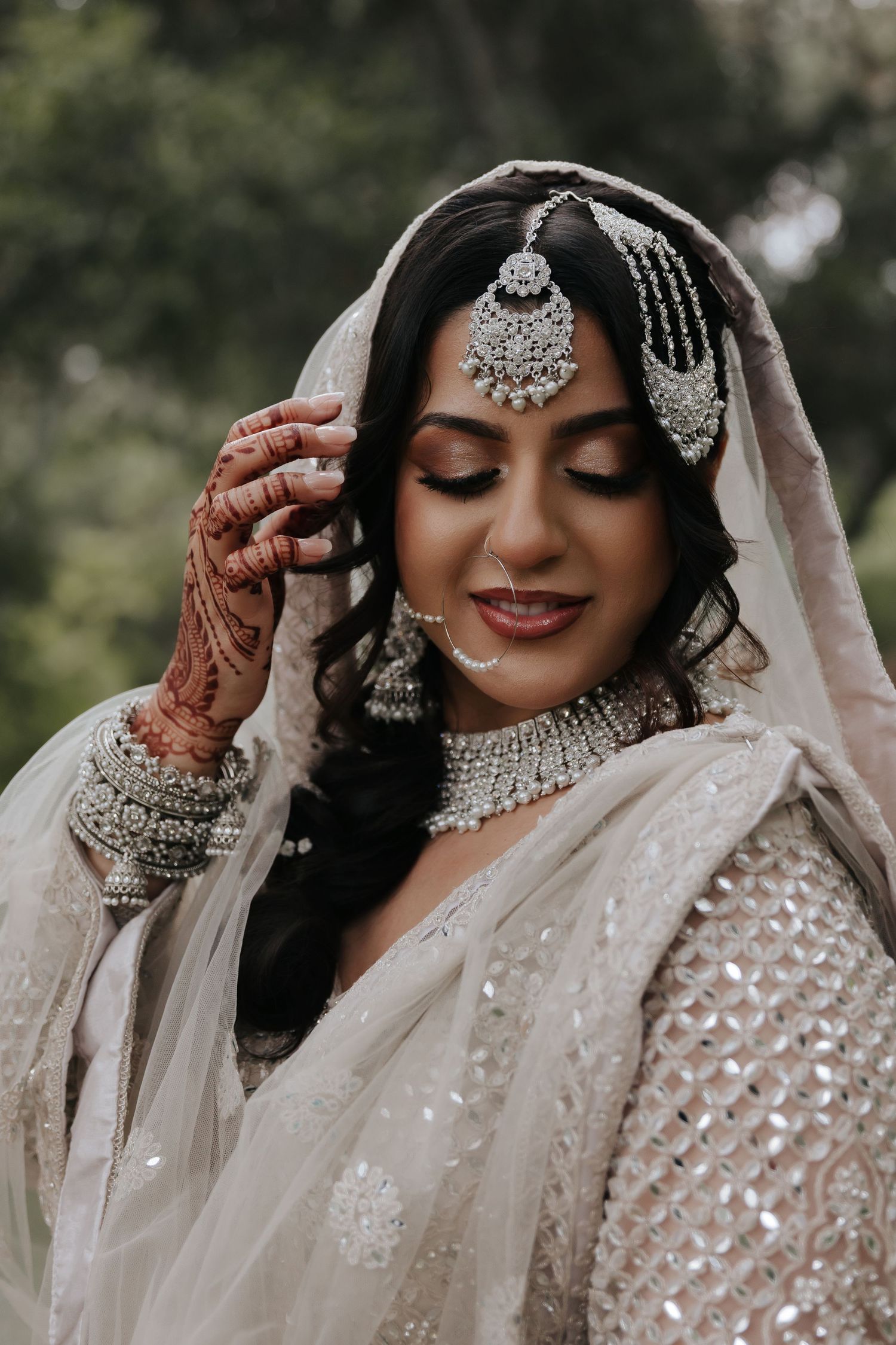 Close-up of bridal jewelry and henna-adorned hands with embellished white wedding attire.