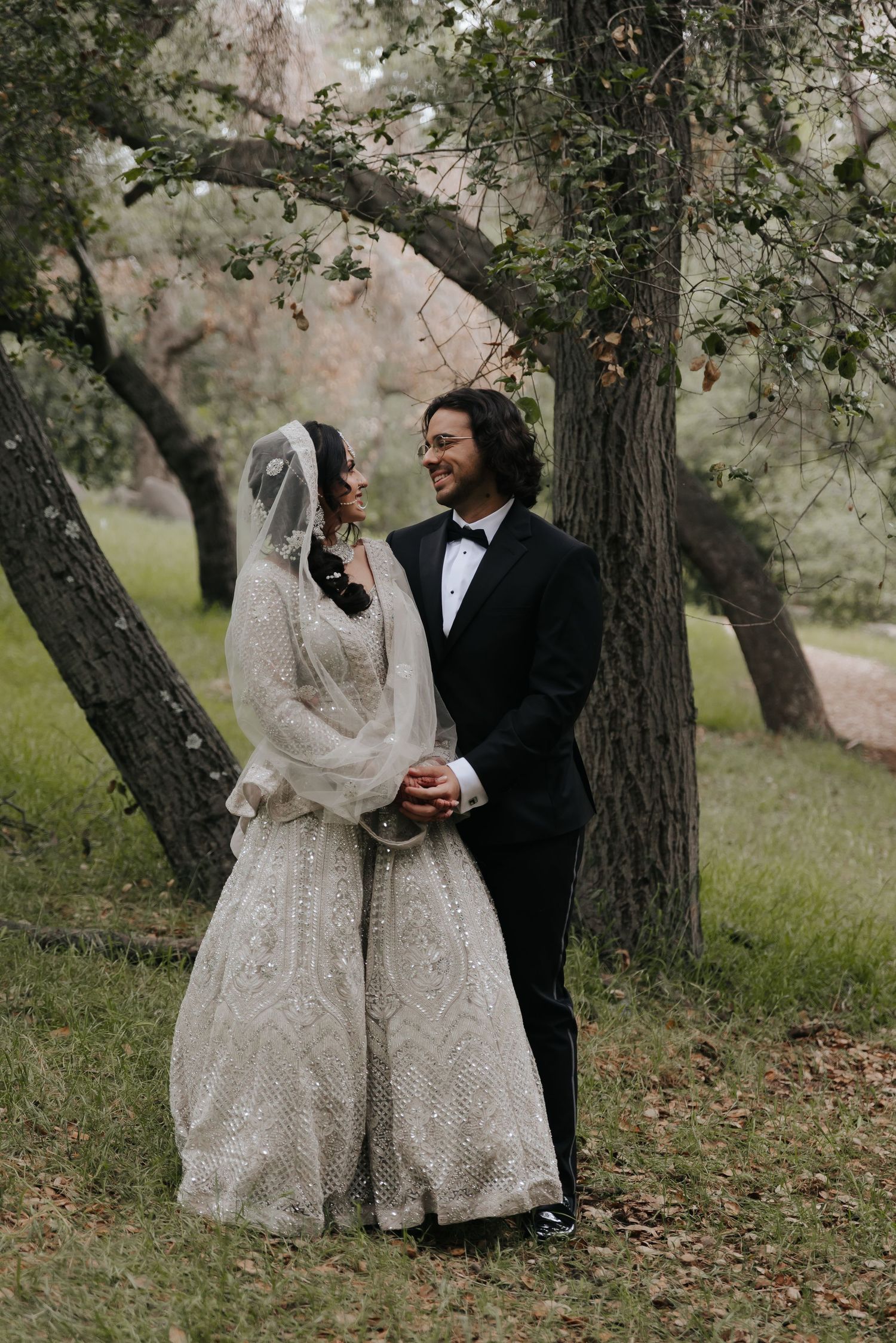 A romantic wedding photo of a couple standing beneath trees on a wooded path.