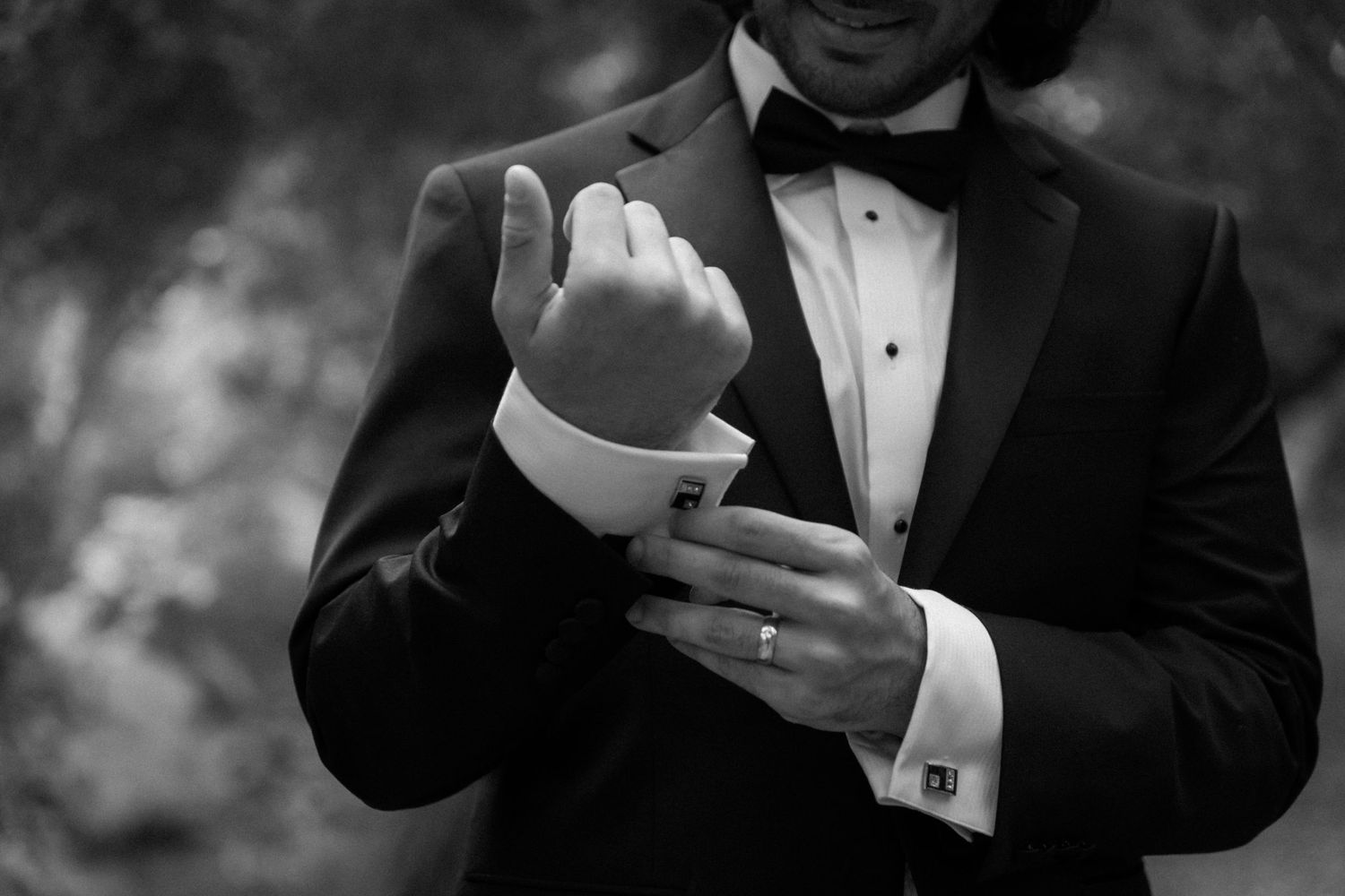 Close-up shot of groom adjusting his cufflinks while wearing a classic black tuxedo.