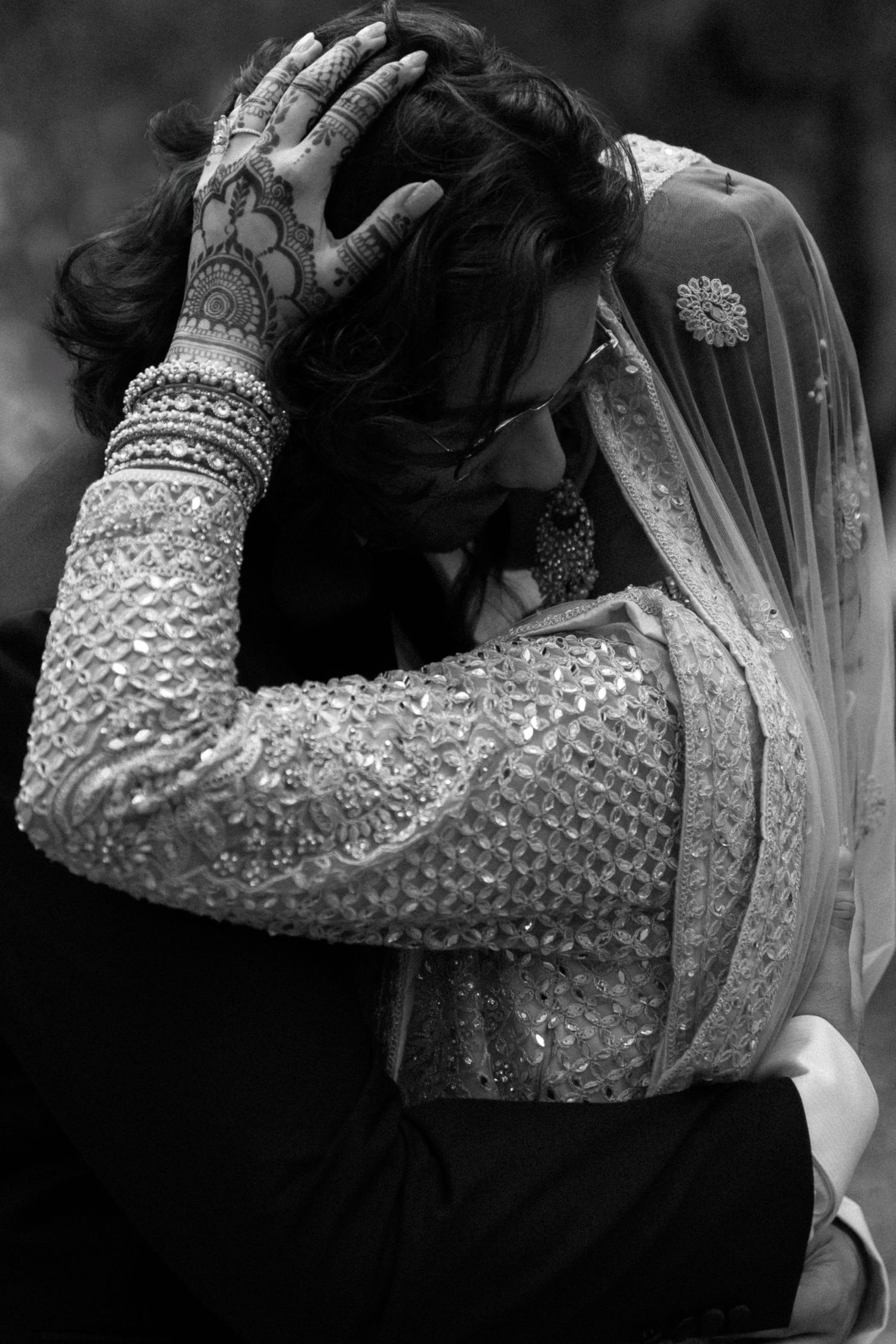 Black and white photo showing detailed henna and jewelry on bride's hand and arm.
