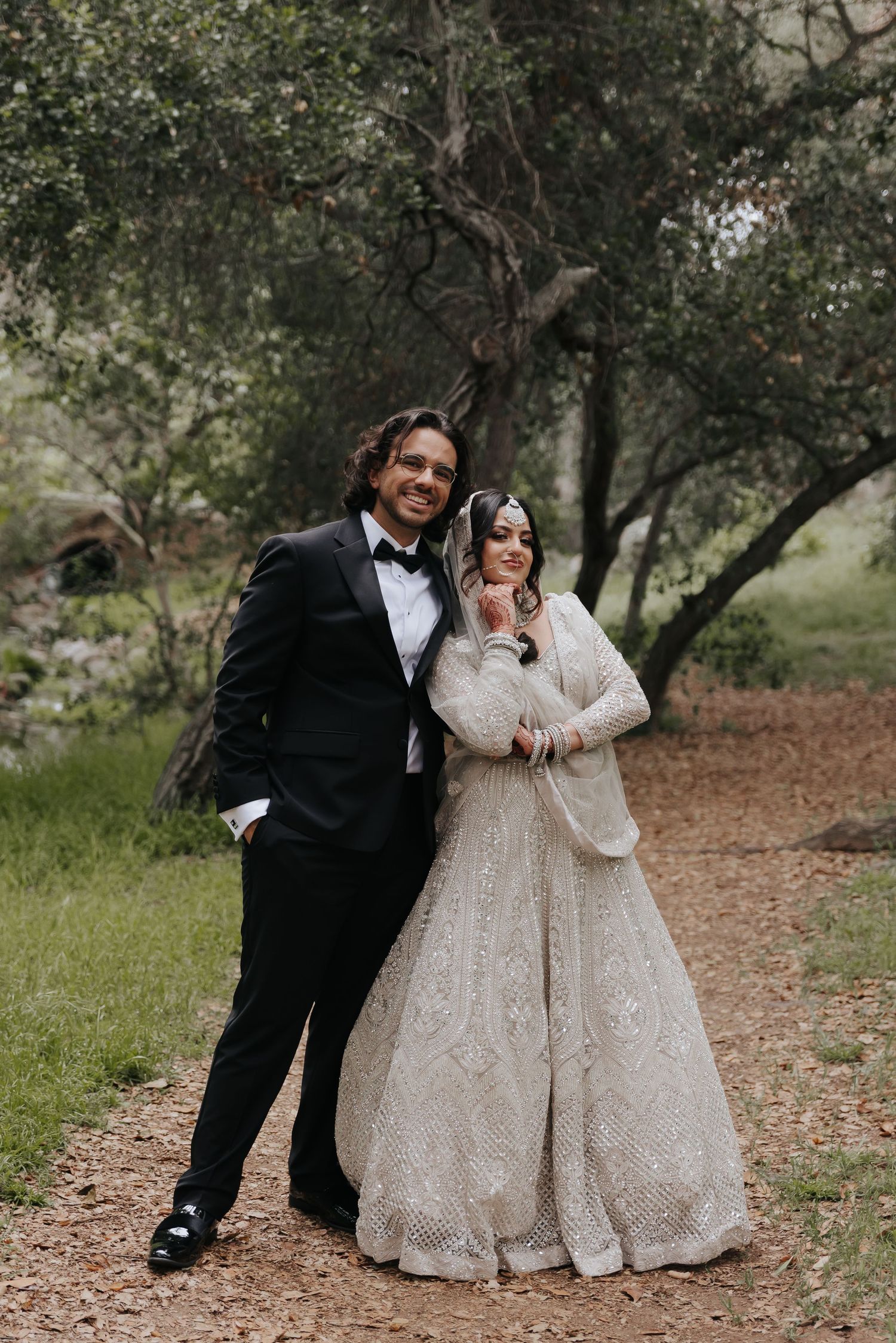 Couple in formal wedding attire standing together on woodland path with natural backdrop.