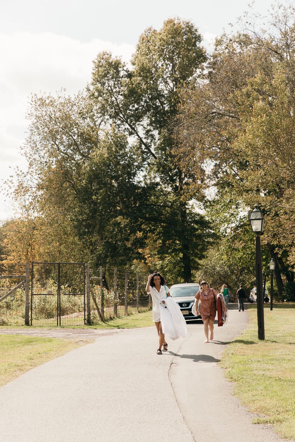 Woman in white dress walking joyfully down a tree-lined path with fall foliage.