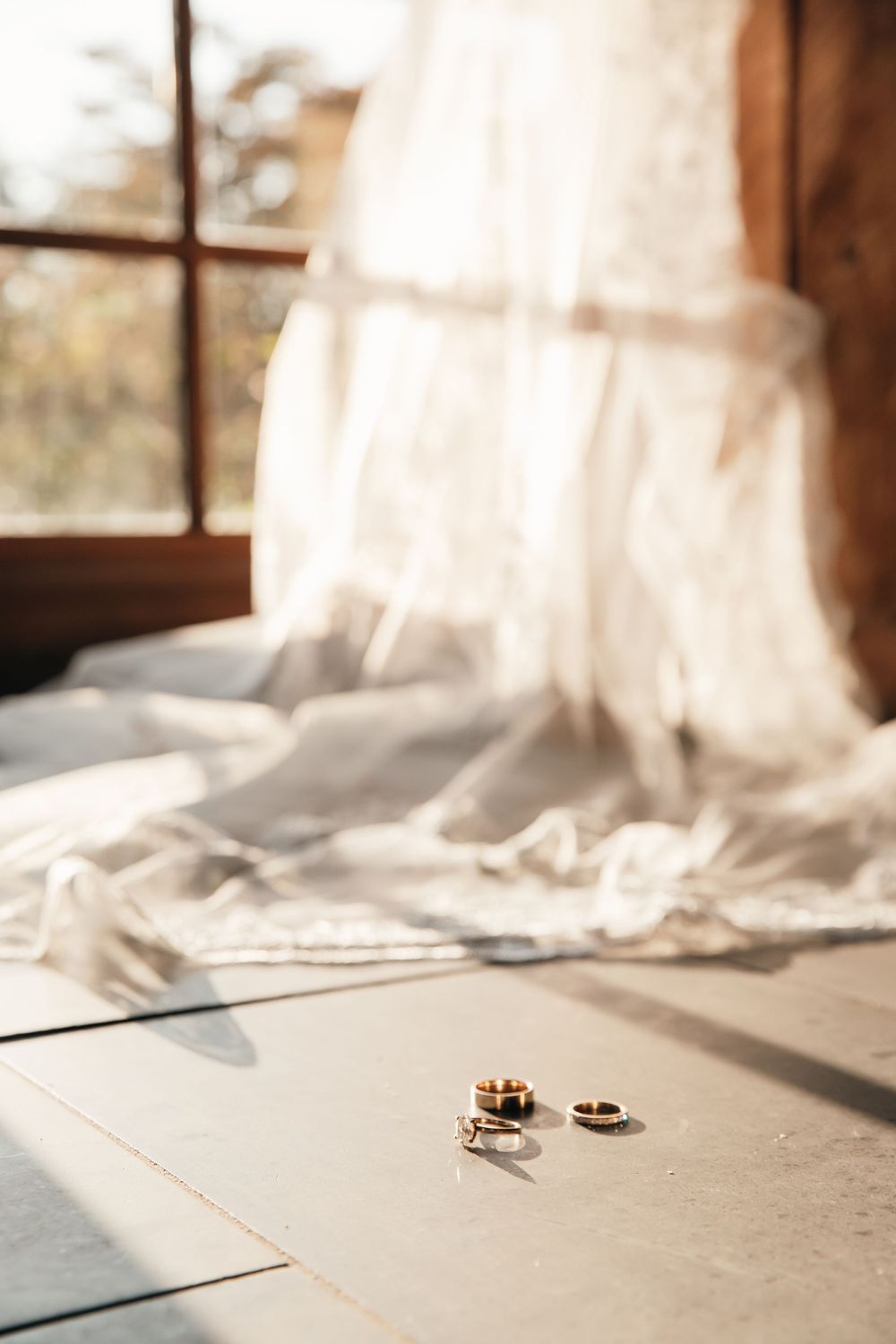 Two wedding rings casting shadows in natural light by a window with flowing white fabric.