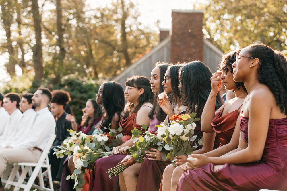 A row of wedding guests sitting in outdoor chairs at a golden hour ceremony watching something in the distance.