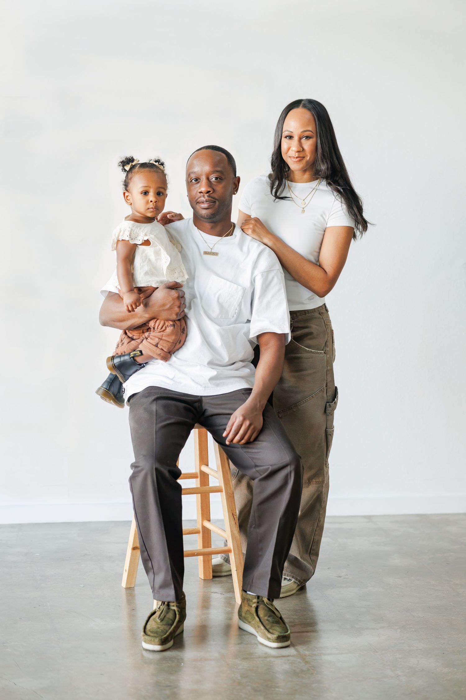 Family poses together against plain white background in minimalist studio in Dallas wearing casual white shirts and neutral paints