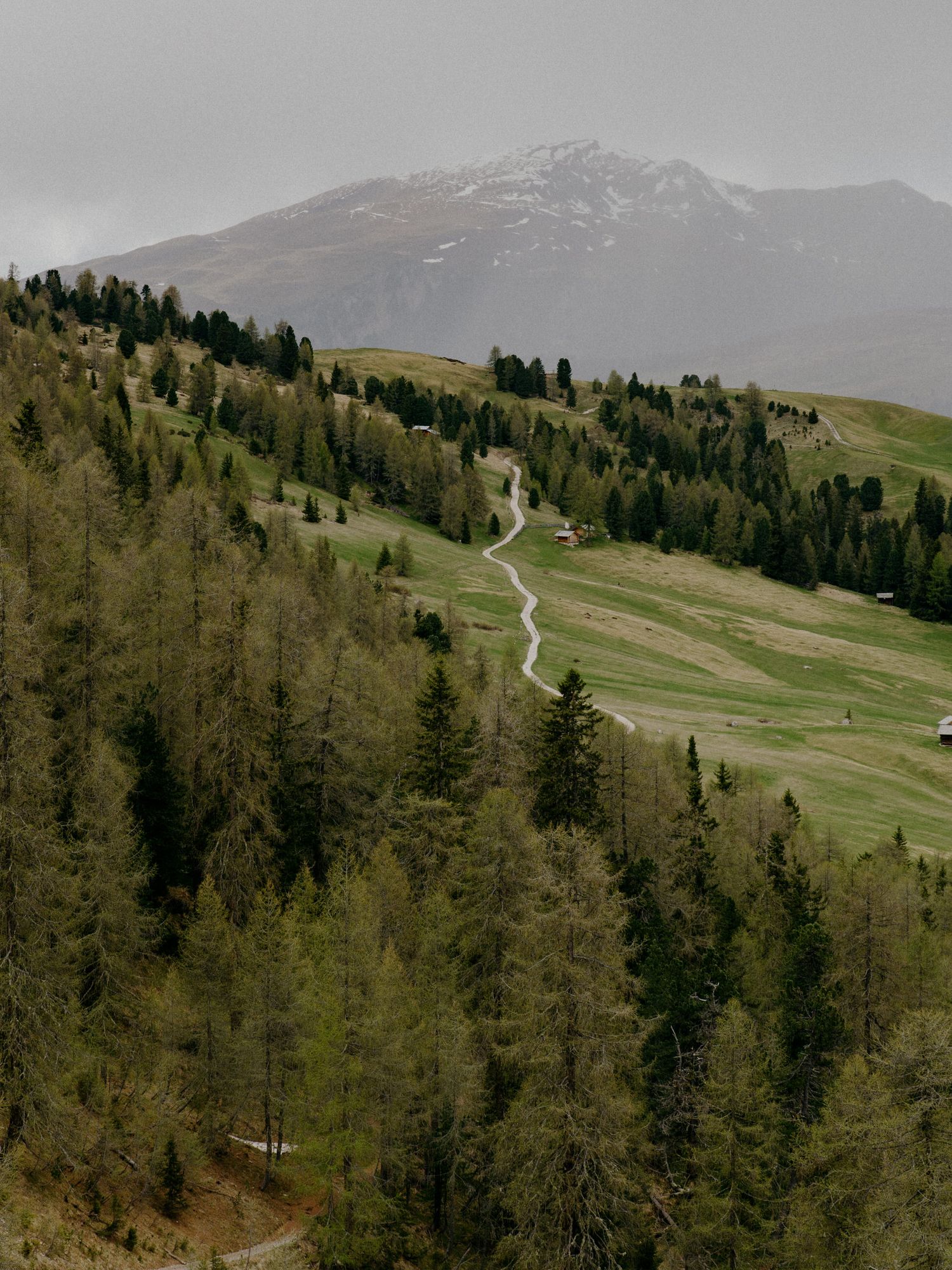 Scenic mountain landscape in the Dolomites with snow-capped peaks rising above green valleys and small alpine villages.