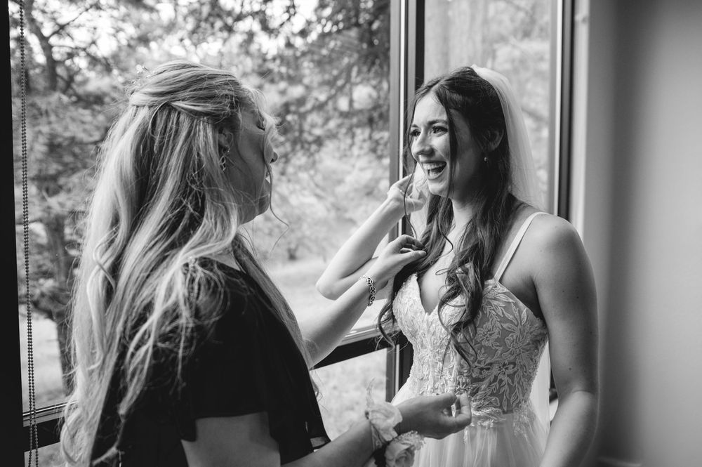 A stylist helps with final touches near a window in a candid black and white wedding preparation moment.