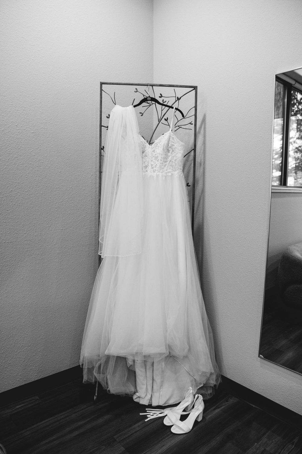 A white wedding gown and veil hanging on display with white high heels placed beneath on a dark hardwood floor.