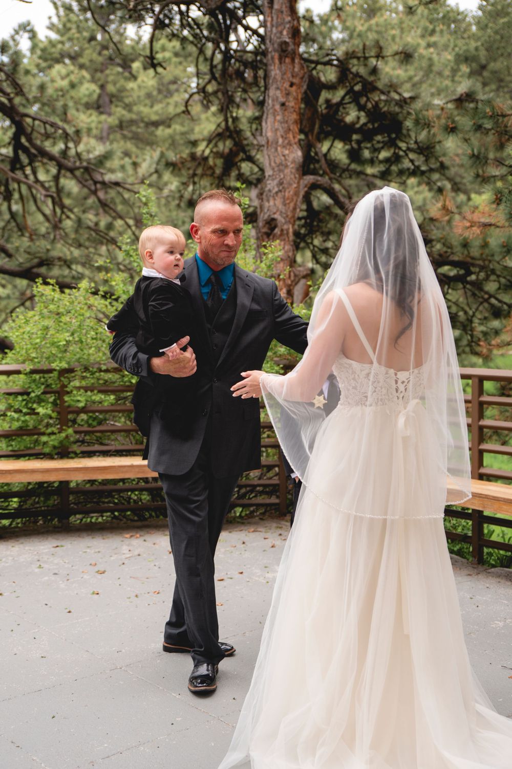 A young boy in a black suit interacting with a bride in a flowing white gown and veil during a wedding ceremony.