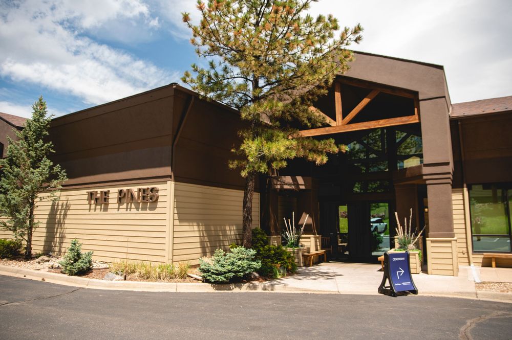 Modern tan and brown building exterior with wood beam accents and glass entrance doors at The Pines location.
