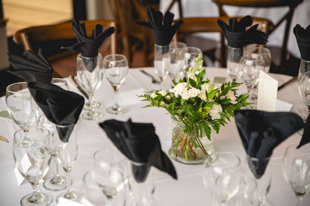 An elegant wedding reception table setting with white flowers, glassware, and black napkins.