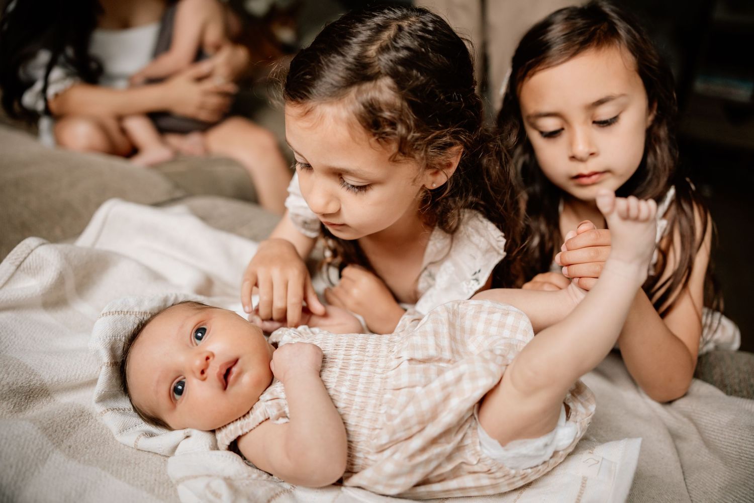 Two young children laying on white bedding next to an alert baby in a pink outfit.