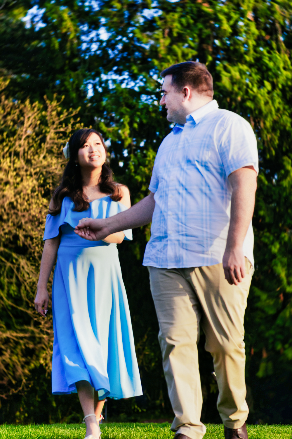 A couple holding hands and smiling while walking together in a garden setting during golden hour.