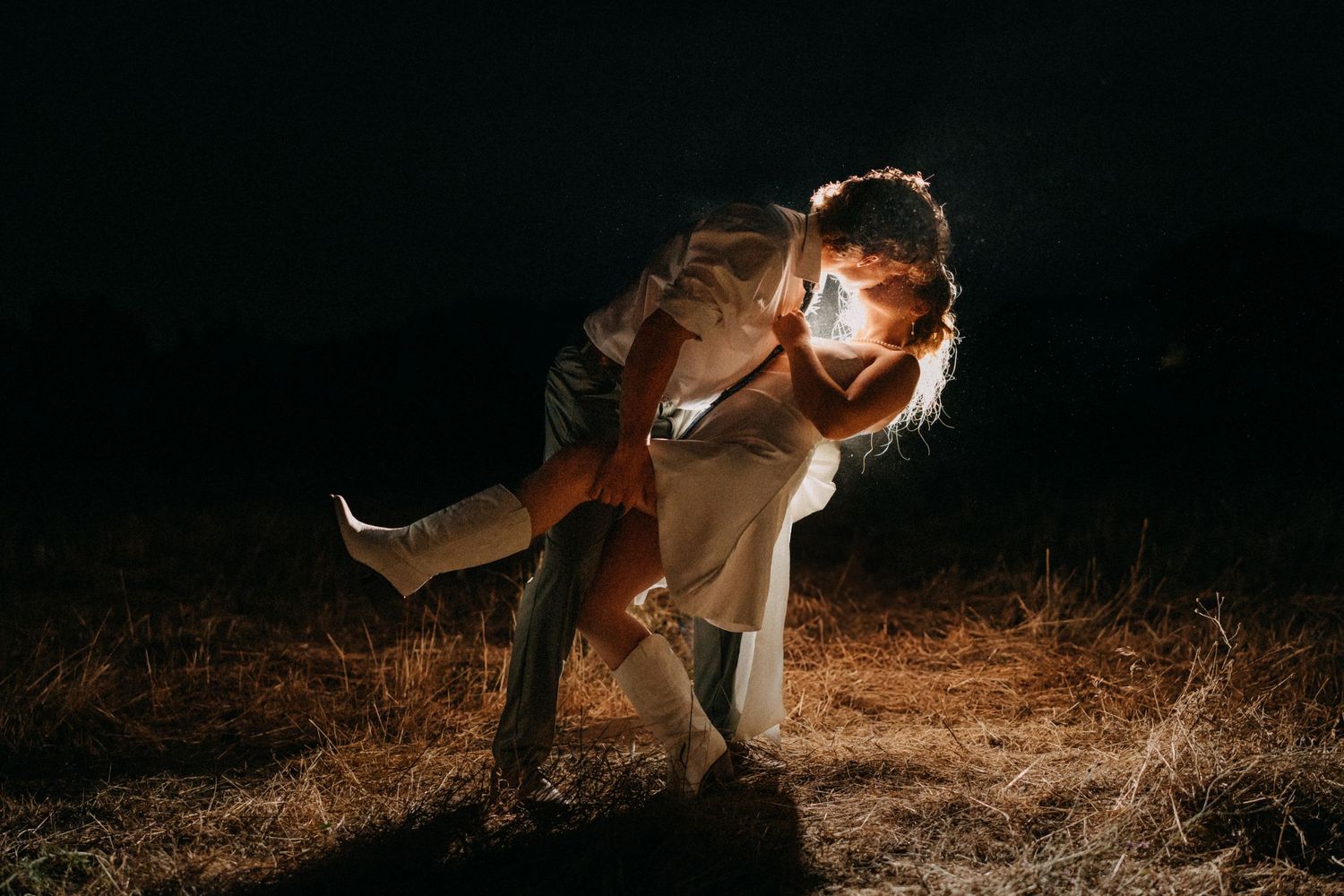 Romantic couple dips dramatically in evening light with hazy backlit glow against dark background.