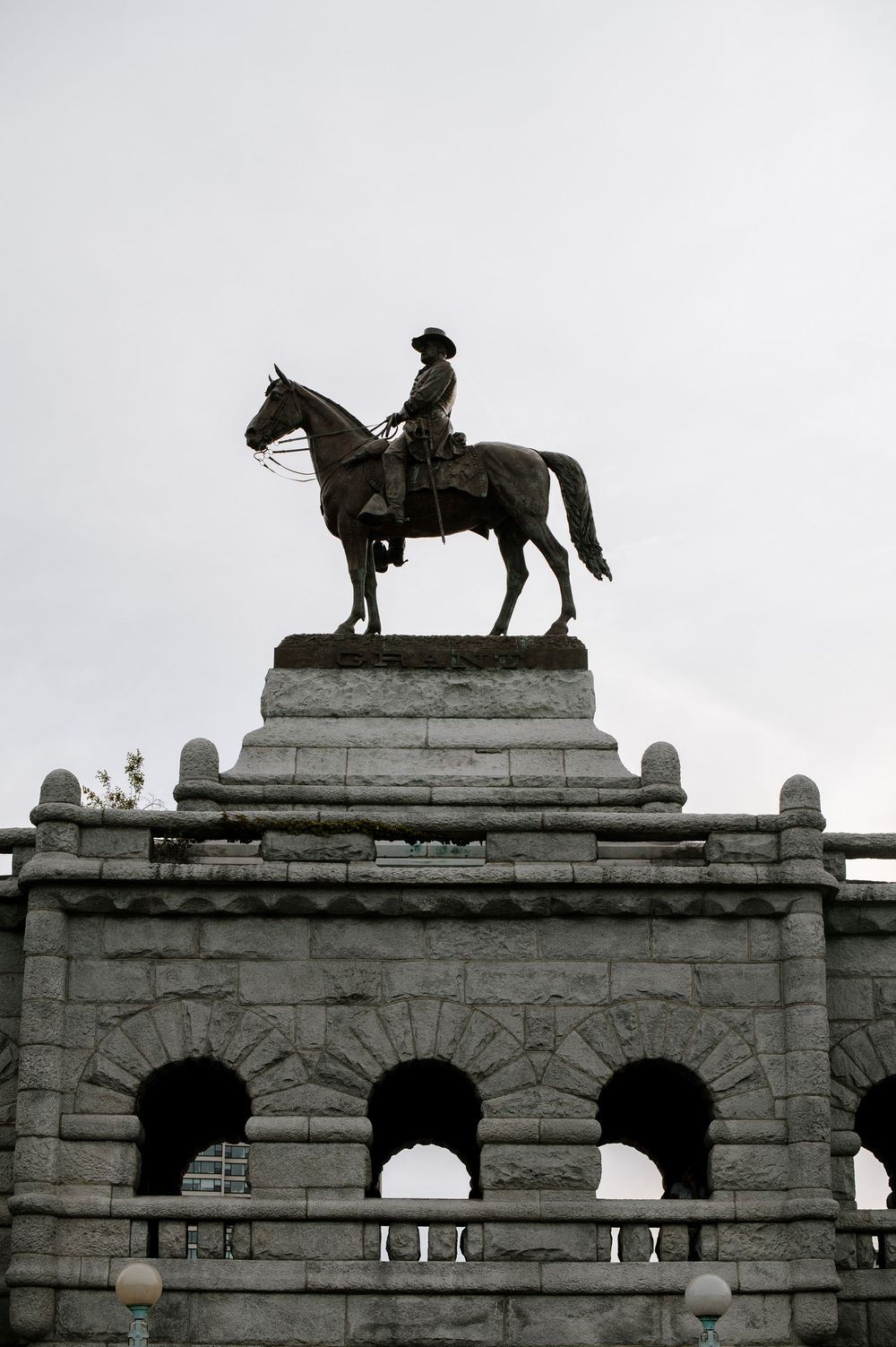 Equestrian statue silhouetted against grey sky on stone archway monument with classical architectural details.