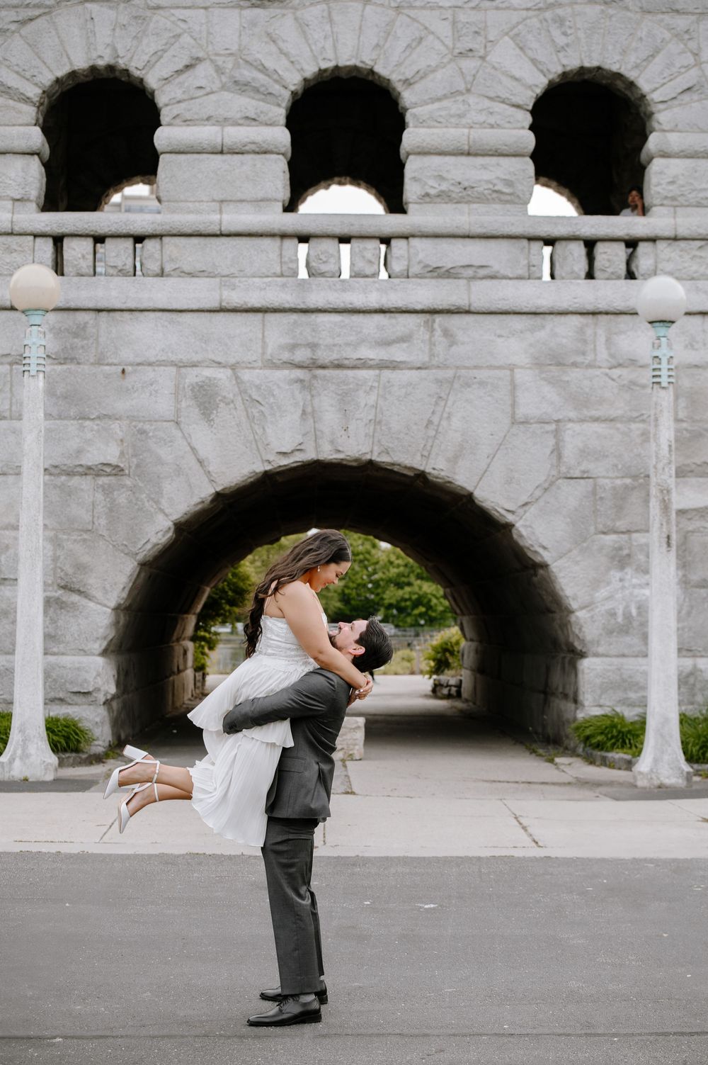 Wedding couple poses creatively under stone arches at a historic building.
