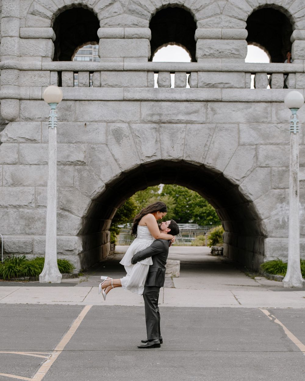 A couple sharing a romantic moment while standing beneath a grand stone archway in an urban setting.