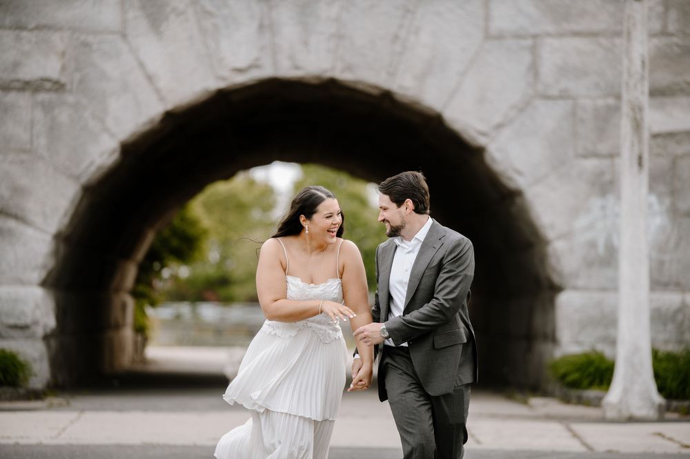 A couple share a joyful moment under a stone archway during their wedding photo session.