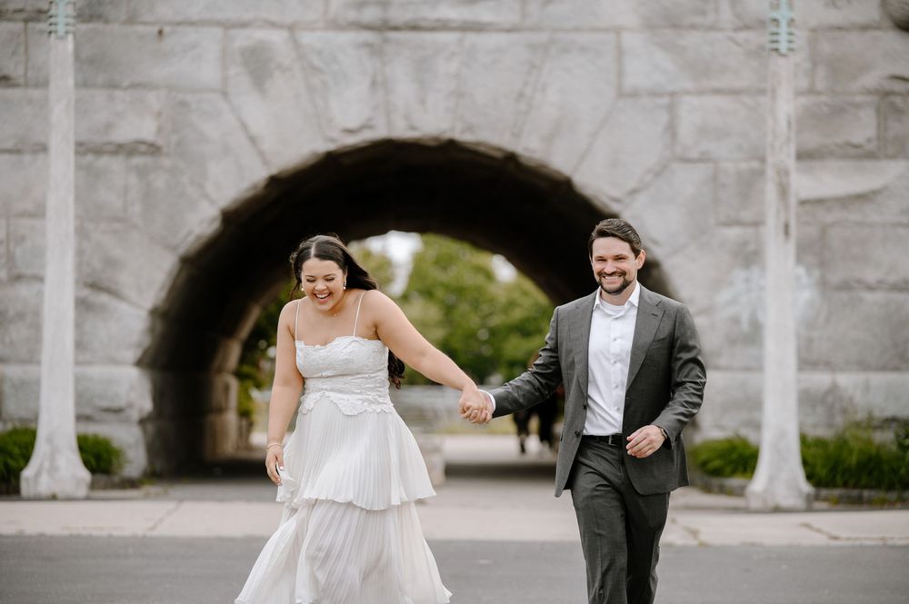 A happy couple run together beneath a stone archway during their wedding celebration.