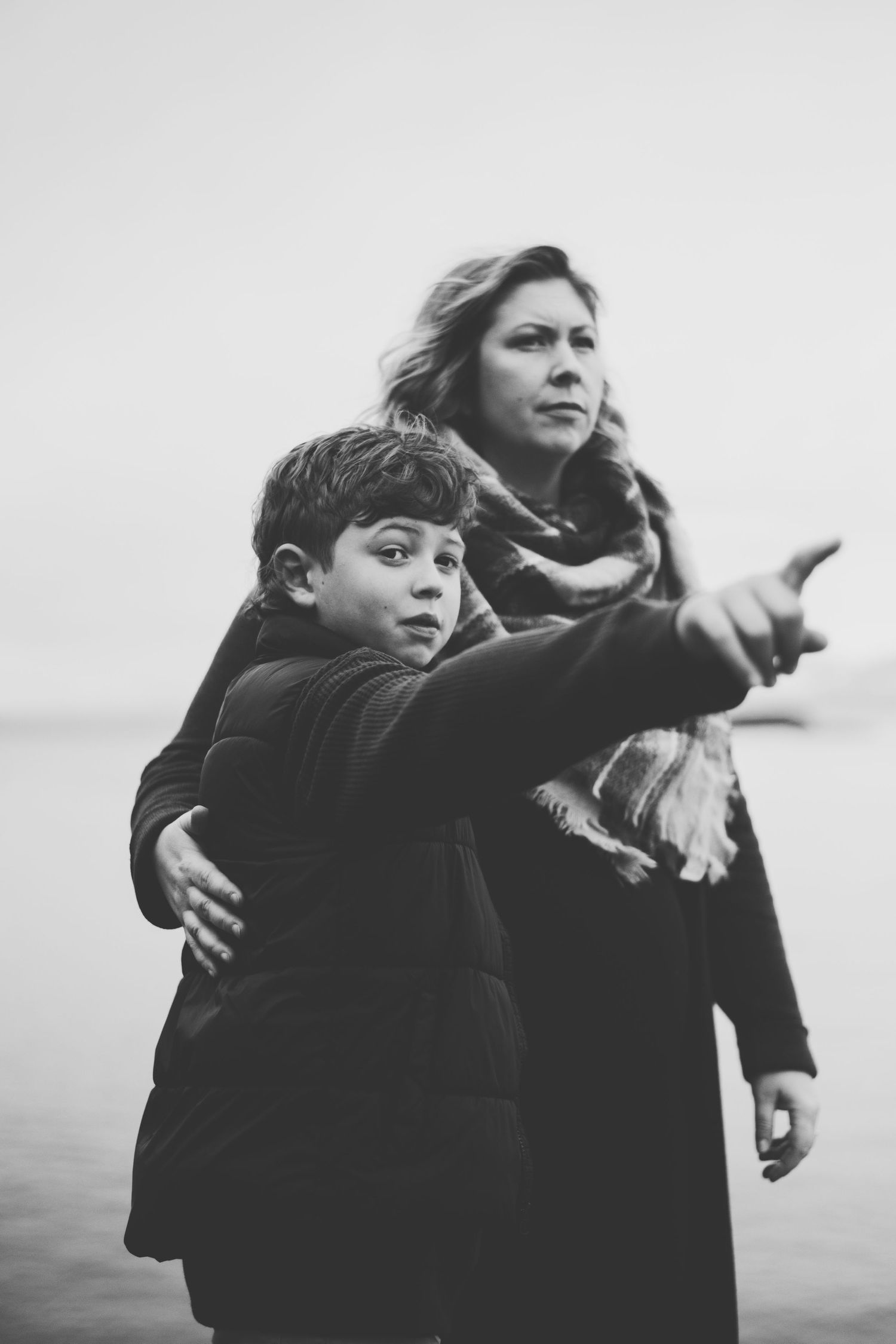 A black and white photo of a mother and son pointing into the distance while standing together outdoors.