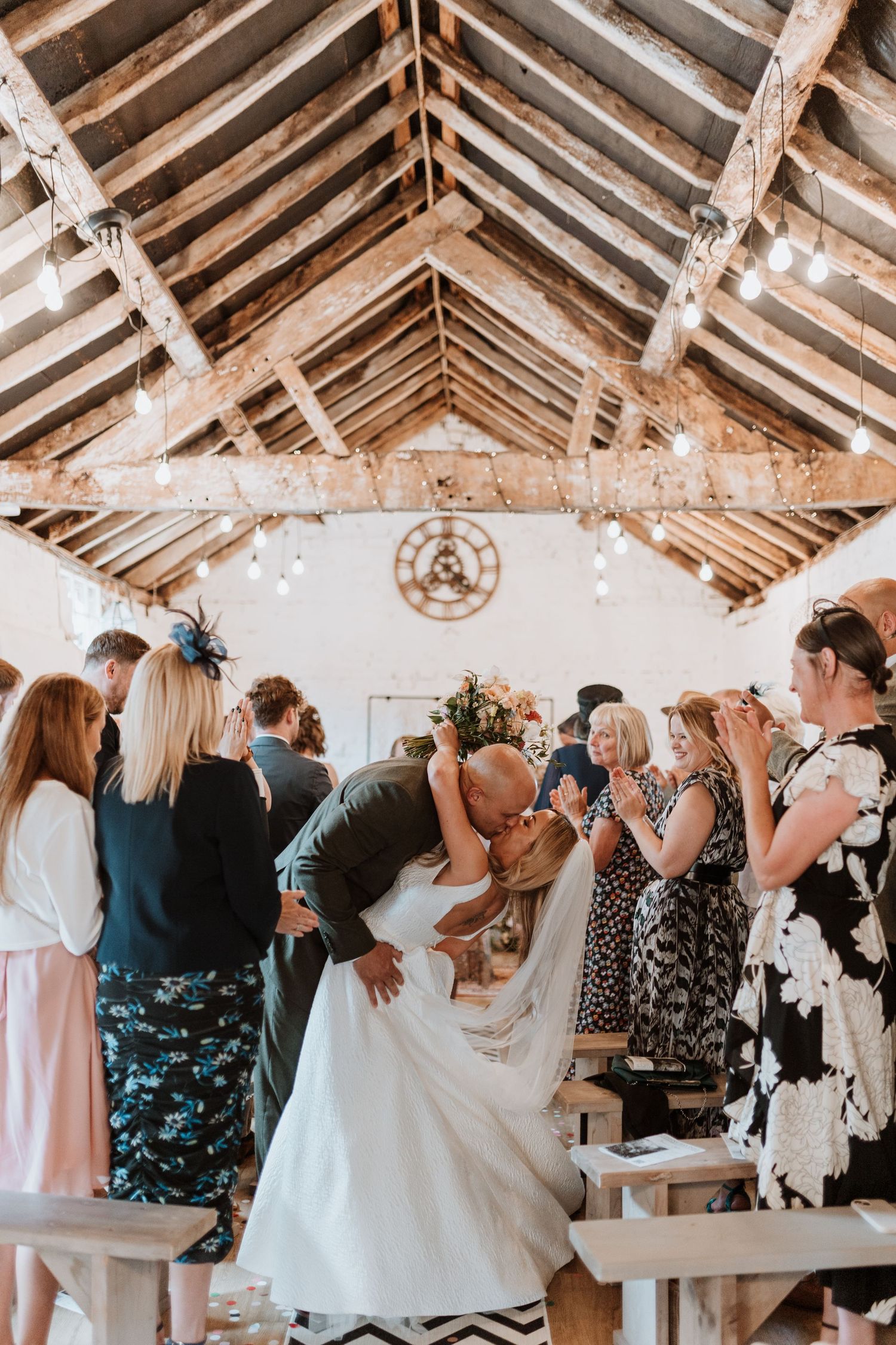 Wedding ceremony taking place in a rustic barn venue with exposed wooden beams and guests gathered around at Stanford Farm.