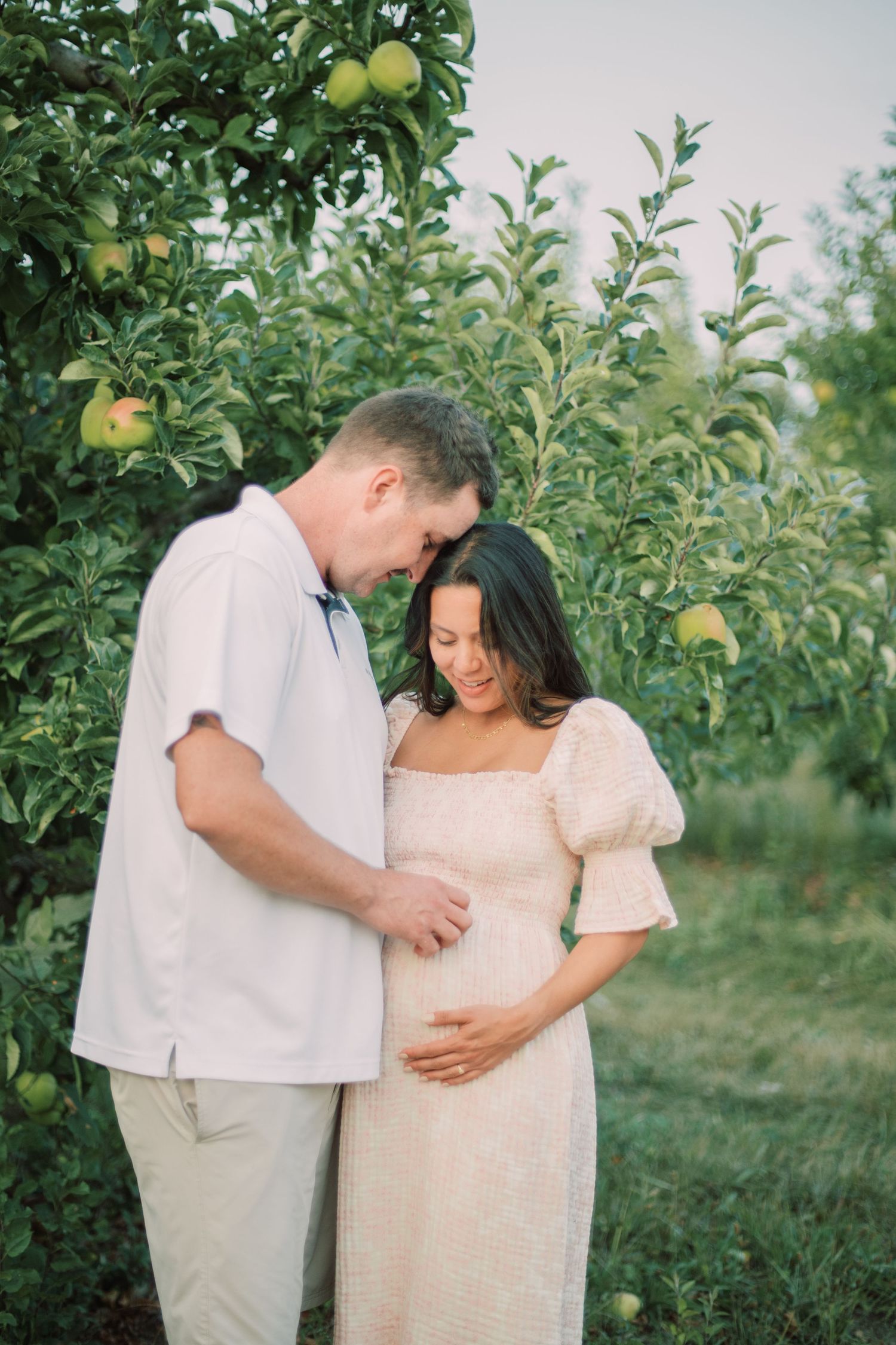 A tender moment between a couple in an apple orchard during a maternity photoshoot.