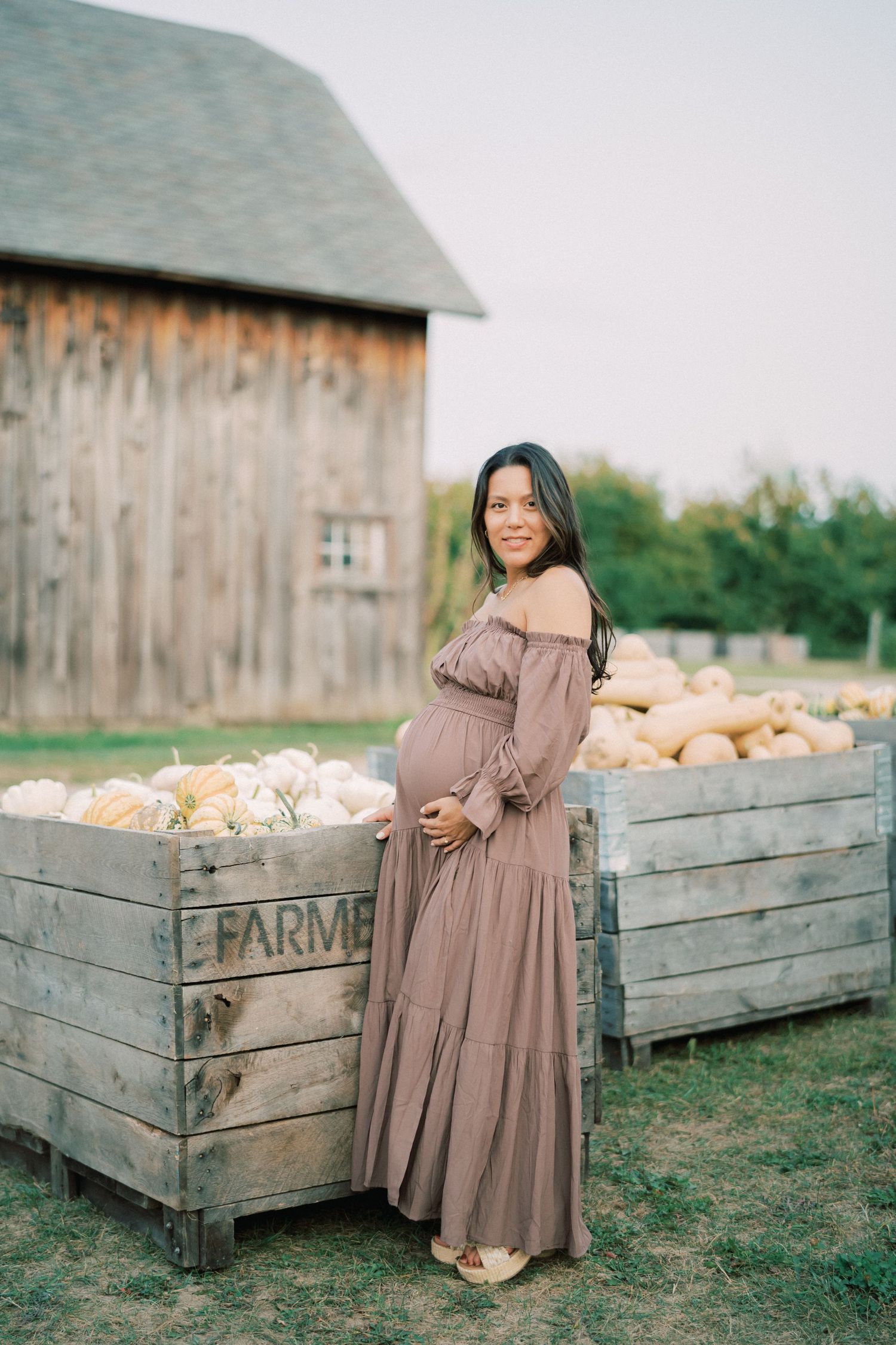Pregnant woman in brown dress posing by rustic farm crates.