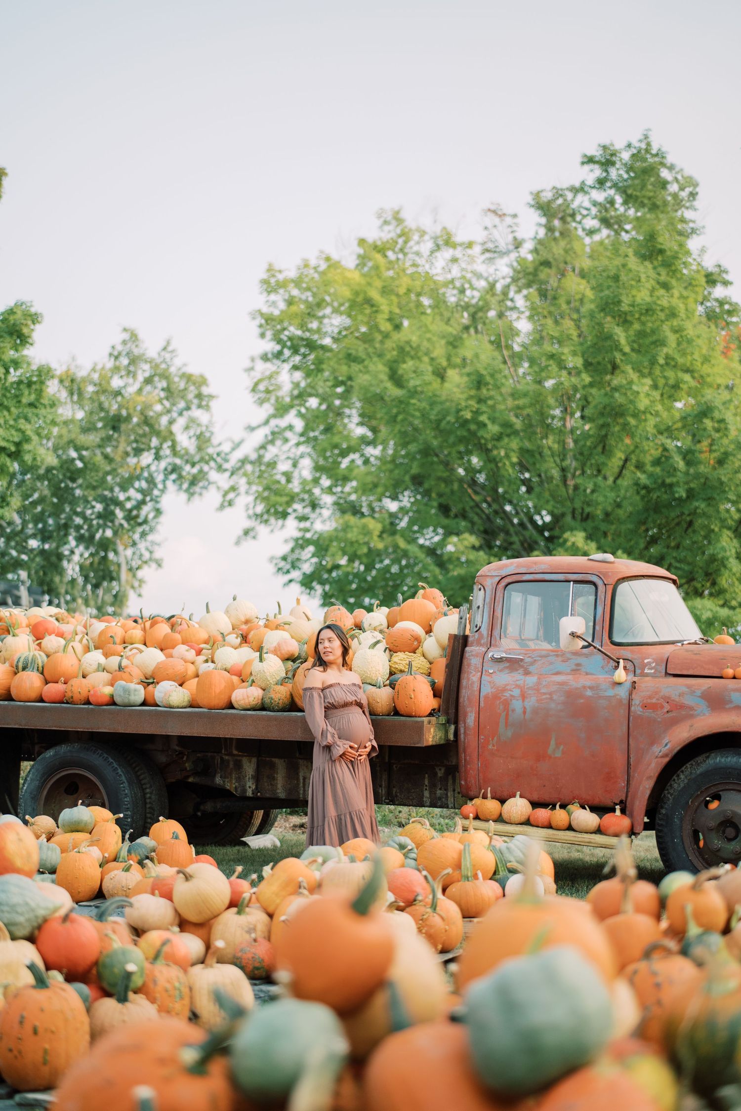 Orange pumpkins surround a vintage red pickup truck in an autumn farm setting.